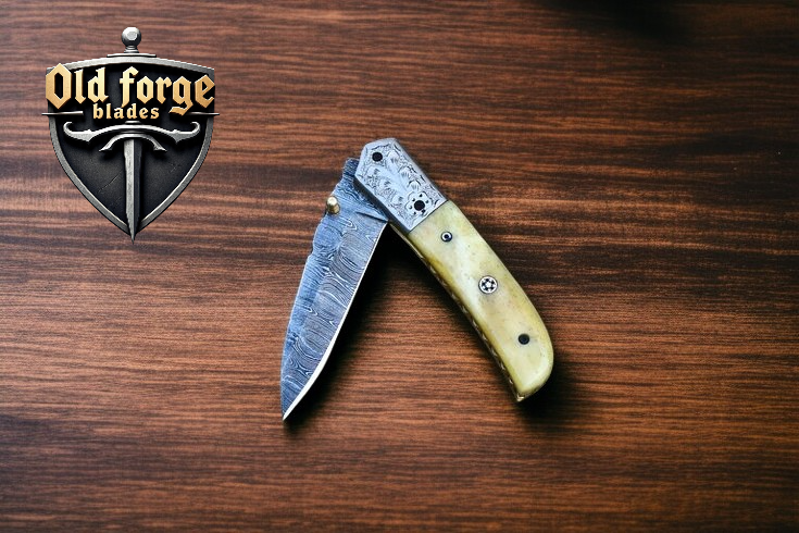 Folding knife with wooden handle on a wooden surface, featuring 'Old Forge Blades' logo.