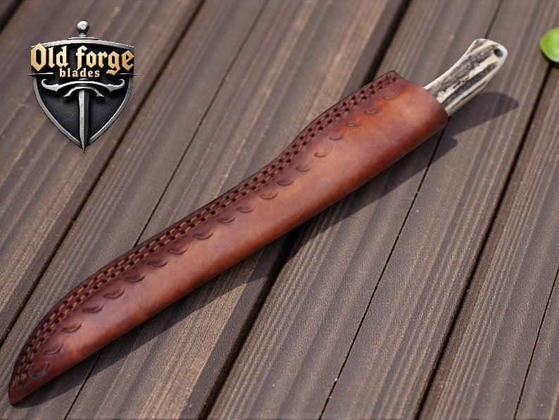 Decorative leather sheath with a blade on a wooden surface, featuring 'Old Forge Blades' logo.